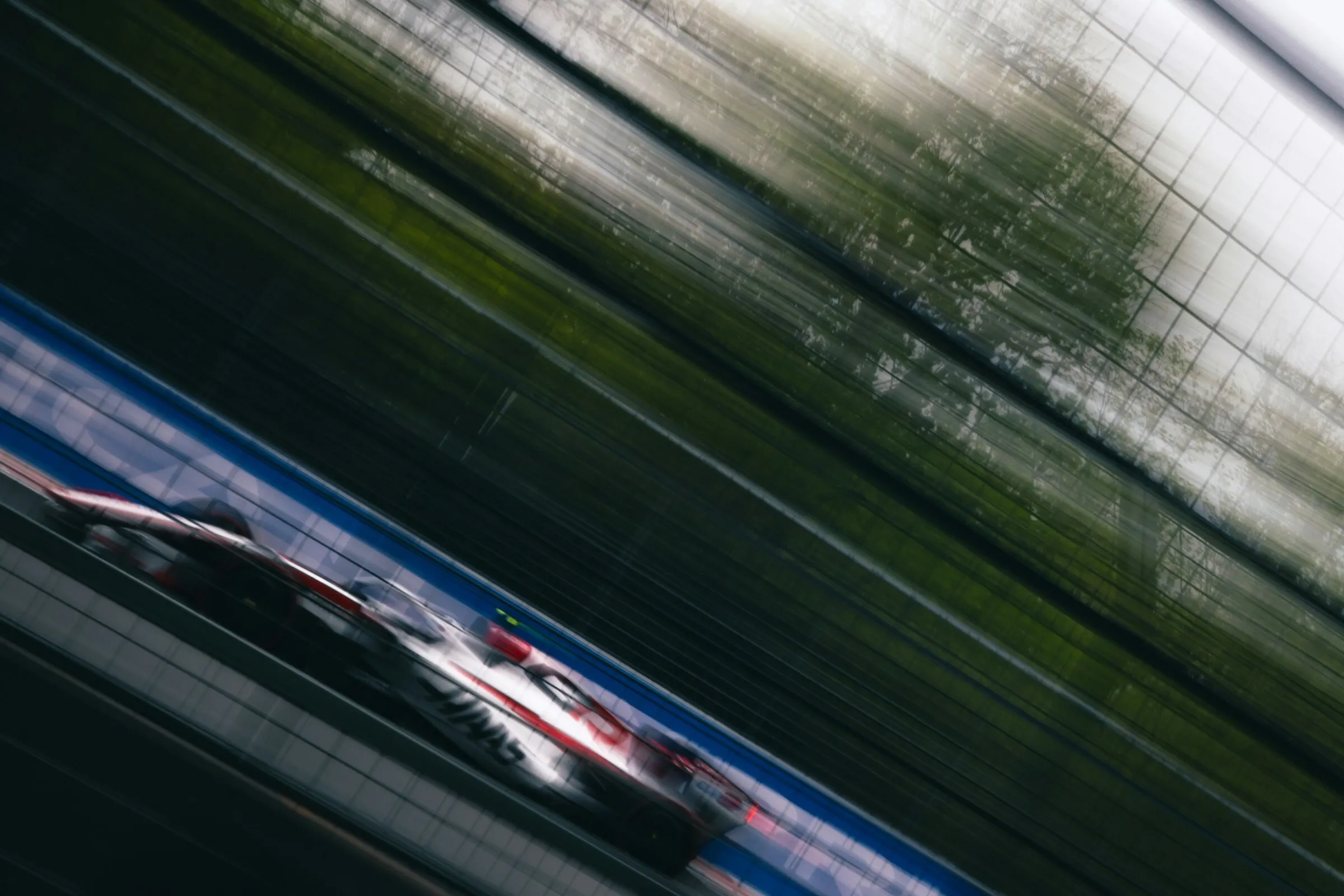 A racing car at speed on a circuit, the background pulled into horizontal motion blur by the panning camera.
