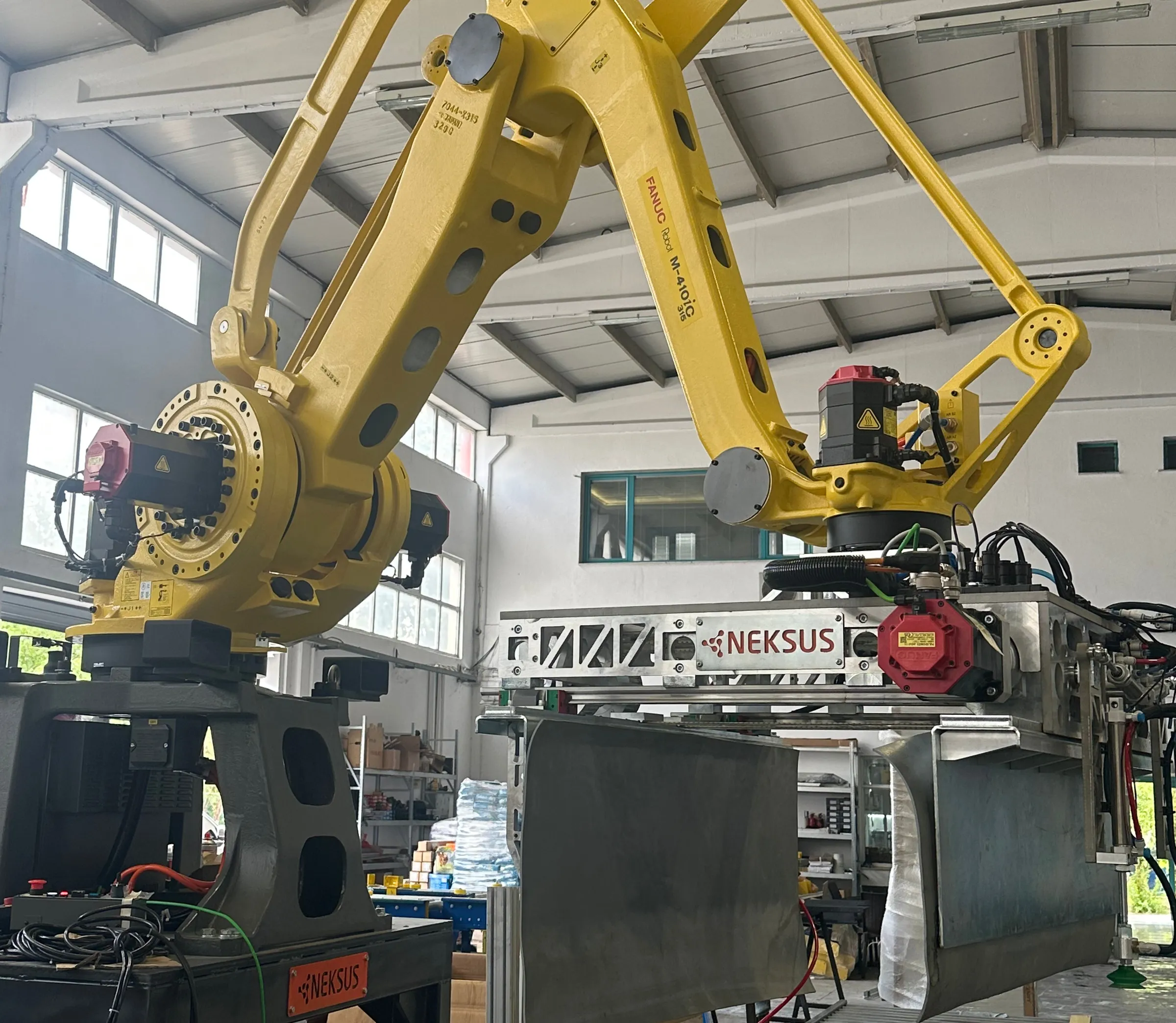 Two large FANUC palletizing robots in the workshop hall, arms raised over a gantry and conveyor.